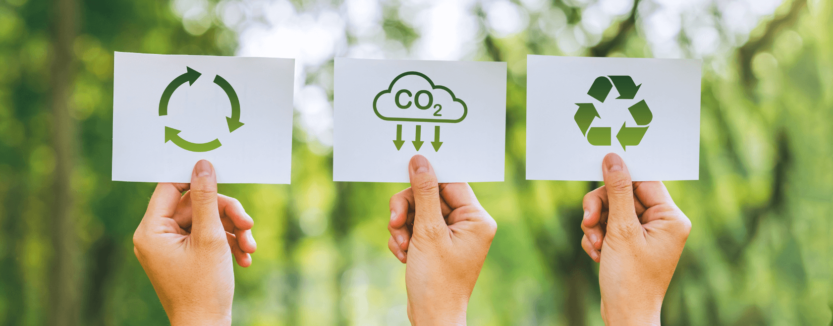 Three hands holding up cards with carbon emissions symbols on them.